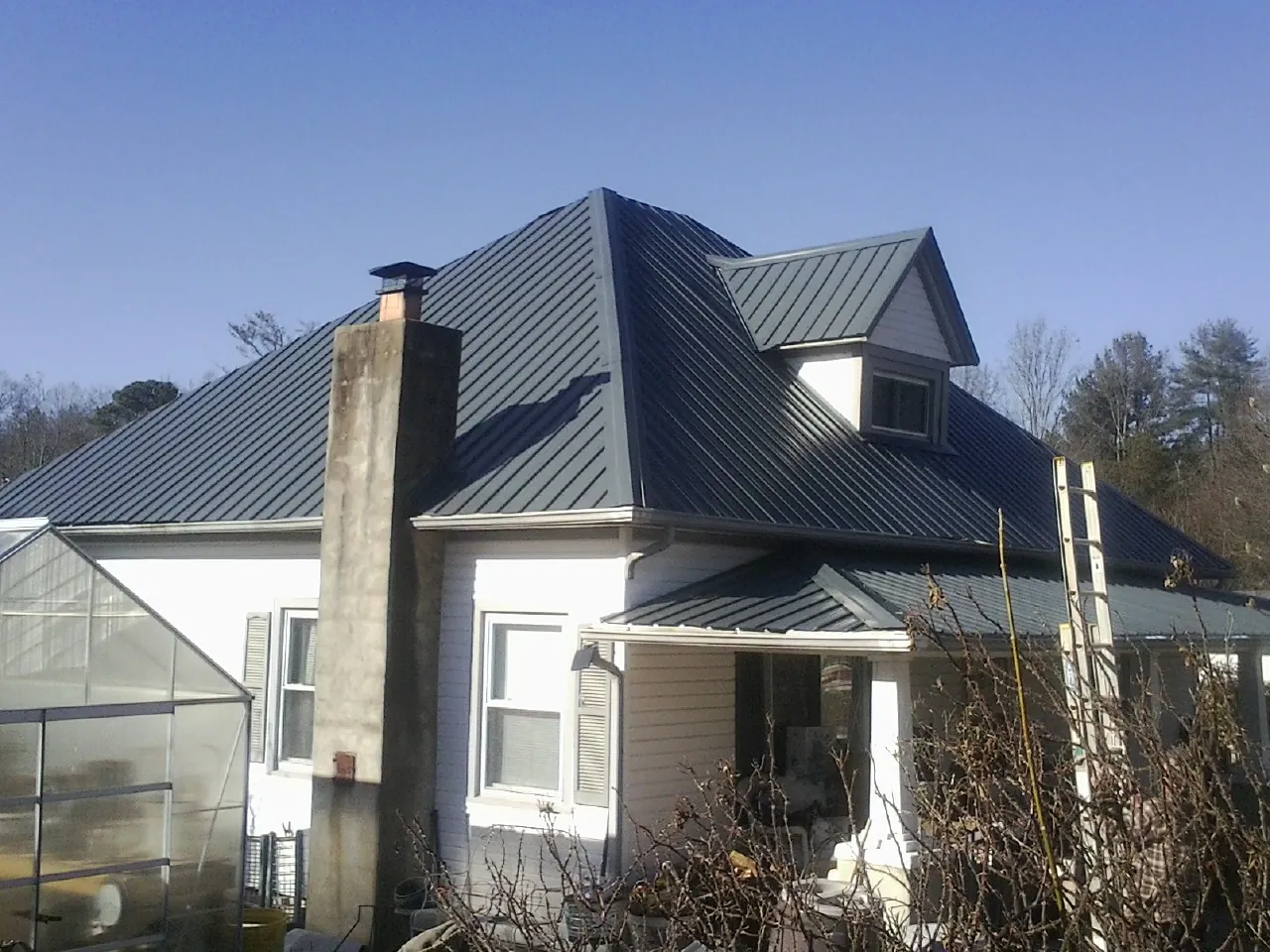 Dark blue standing seam metal roof on a white farmhouse with dormer — Slate & Tile Roof Repair by Roofing Brothers in Saulsbury