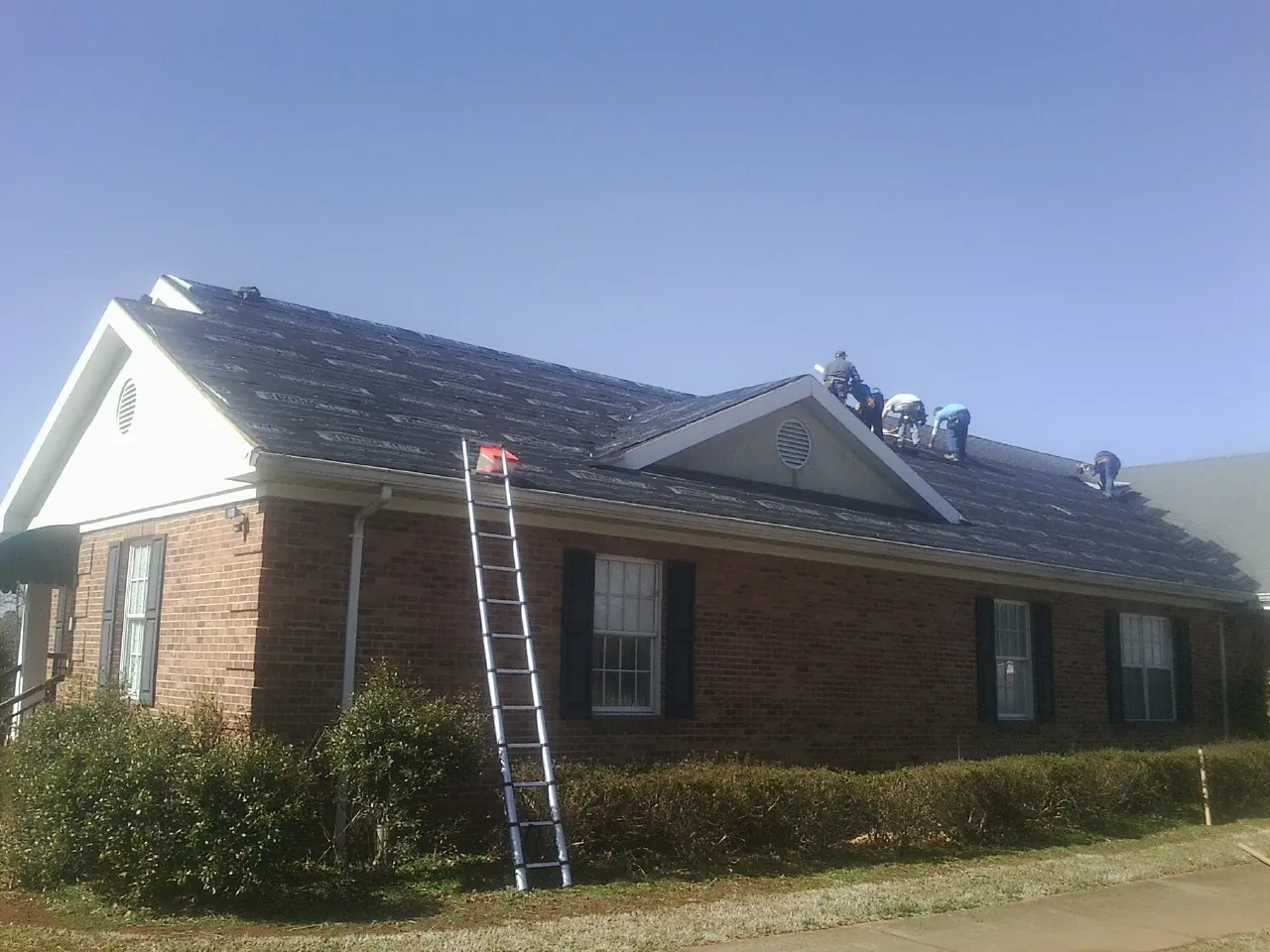 Crew tearing shingles off a brick ranch roof with a ladder set — Metal Roof Repair work by our crew in Saulsbury