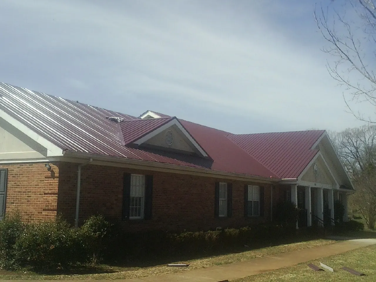 Red metal roof with gabled entries on a long brick building, from a Hail Damage Roof Repair job in Saulsbury