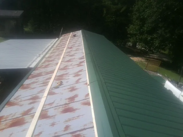Old rusted panels beside newly installed green metal roofing — Wind Damage Roof Repair by Roofing Brothers in Saulsbury