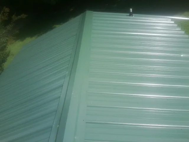 New green metal panels meeting at the ridge of a roof — Flat Roof Repair work by our crew in Saulsbury