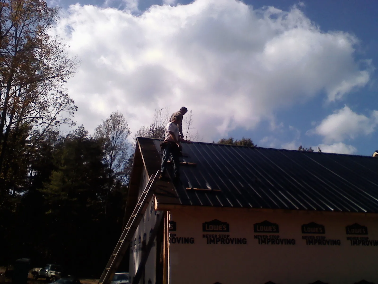 Roofer fastening dark metal panels high against a cloudy sky, from a Roof Inspection job in Saulsbury