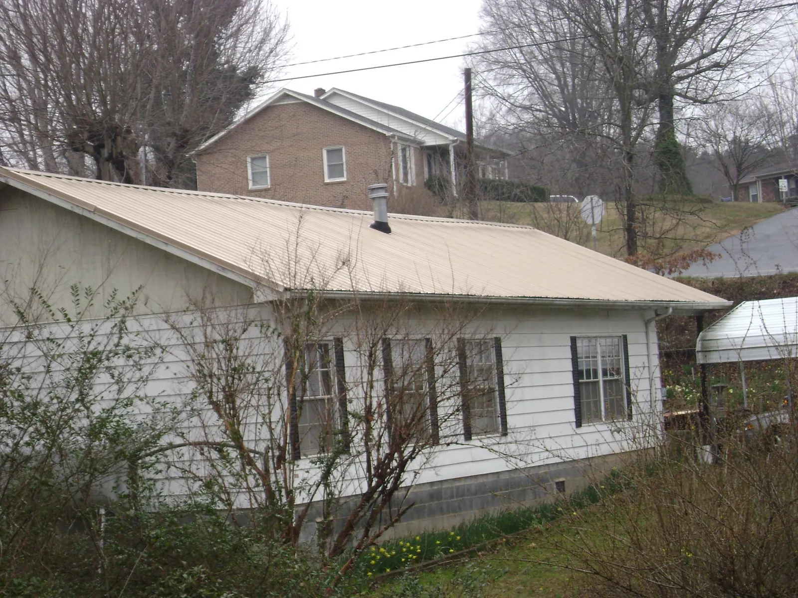 Tan metal roof on a white sided house set into a hillside — Commercial Roofing by Roofing Brothers in Saulsbury
